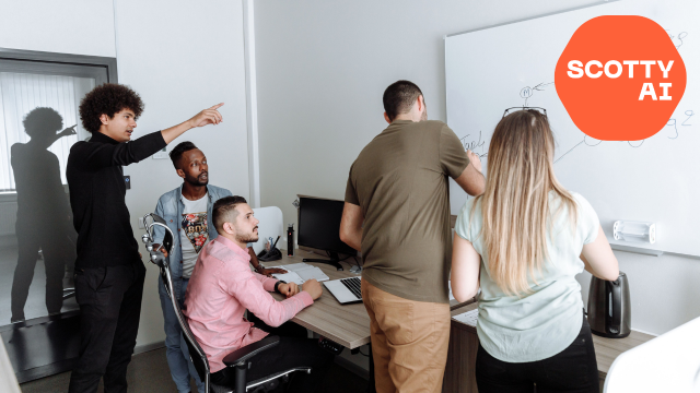 People in meeting room pointing at board with planning plus Scotty AI logo